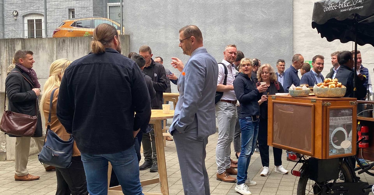 Personen aus verschiedenen Unternehmen beim gemeinsamen Stehfrühstück draußen und beim netzwerken